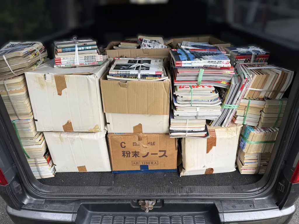 広島市安芸区でお引き取りした雑誌・ムック・本を、当店のハイエースの荷室に積み込んだところ。段ボール箱が下段と中段に並び、その上と両脇に、紐やバンドで束ねた雑誌やムック、文庫・新書サイズの本が積まれている。中央上段と右上の束には学研のムックの背が見える。引越し前の片づけで、買取できたものも買取できなかったものも、すべてお引き取りした積み込みの様子