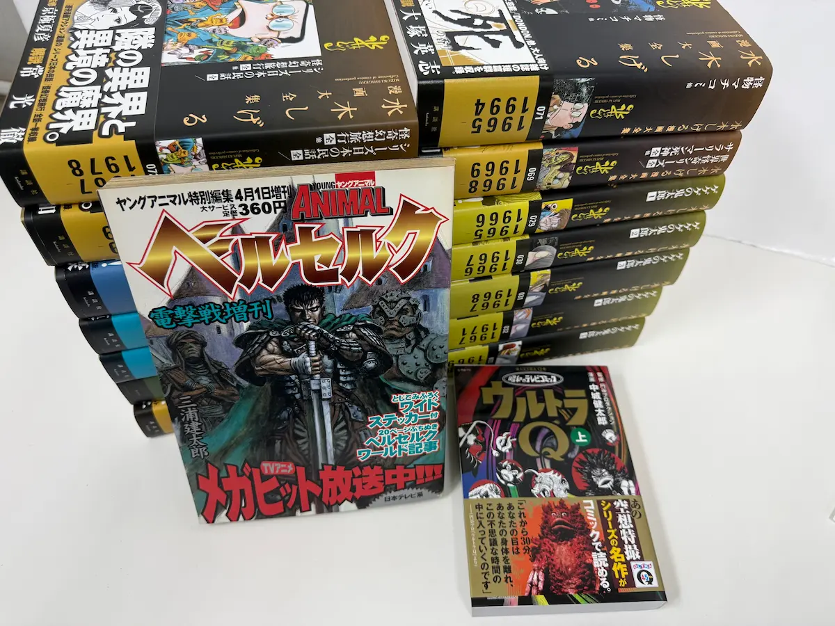 本日お預かりした蔵書——白泉社ヤングアニマル特別編集『ベルセルク電撃戦増刊』（三浦建太郎、TVアニメ放送中の帯付き）、光文社文庫『ウルトラQ 上』、奥に講談社『水木しげる漫画大全集』の背表紙が並ぶ