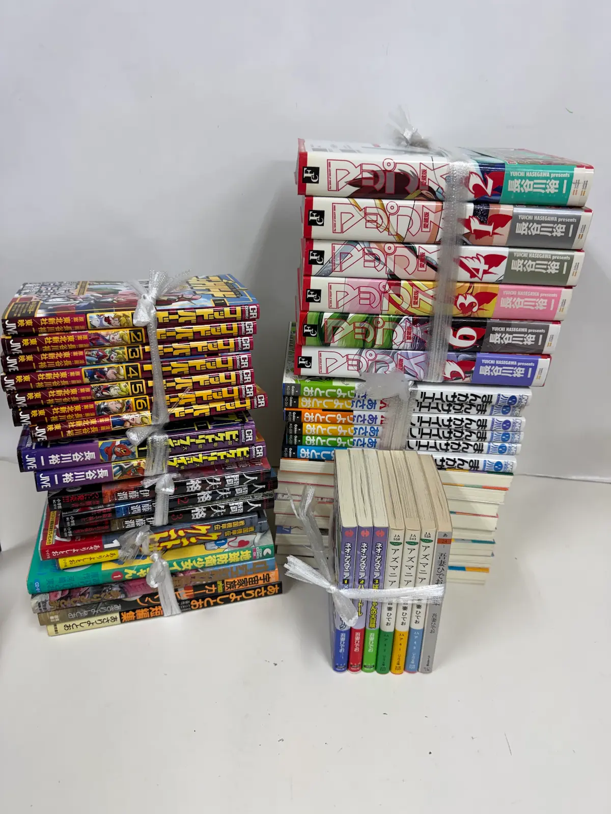 広島市安佐南区のリピーター様からお譲りいただいた漫画を、呉の事務所に持ち帰ってシリーズごとに三つの束に分け、それぞれビニール紐で縛ったところ。左と右に横積みの束、手前に立てた状態の束が並ぶ