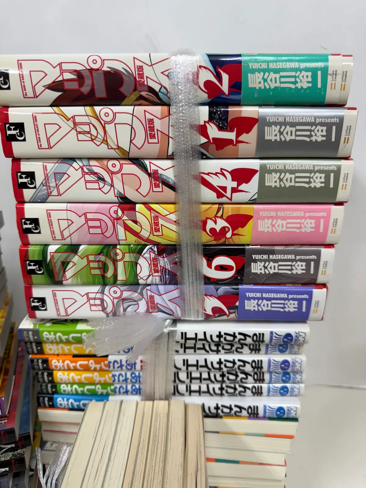 事務所で束にした横積みの背表紙。上半に長谷川裕一『マップス』愛蔵版の6冊がSoftbank CreativeとThe Saga of GALAXY LEGEND、YUICHI HASEGAWA presents の表記とともに並び、下半にあさりよしとお『まんがサイエンス』学研の白と青の背がKG-004、KG-006などの管理番号とともに続く