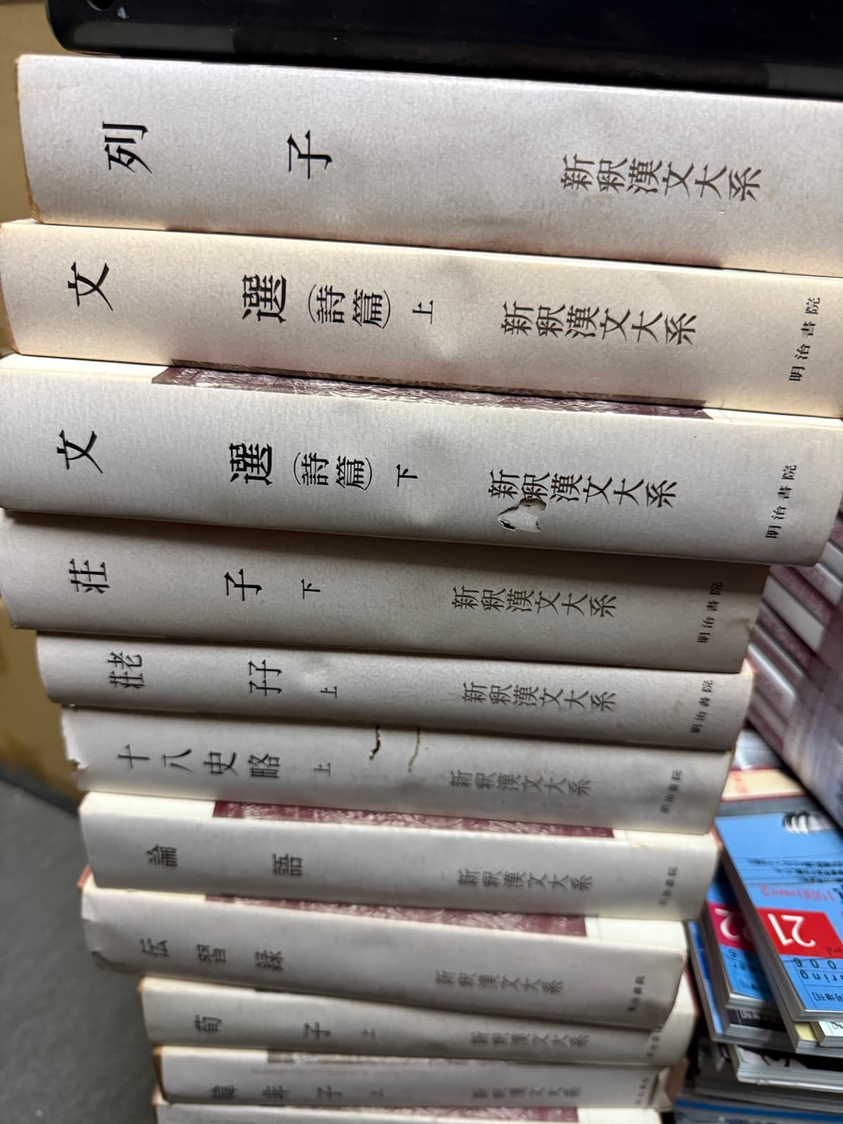 廿日市市出張買取で入荷した明治書院『新釈漢文大系』の背表紙が並んだ様子。列子、文選詩篇上、文選詩篇下、荘子下、孟子上、十八史略上、論語、伝習録、荀子上、韓非子などの巻が縦に積まれている。