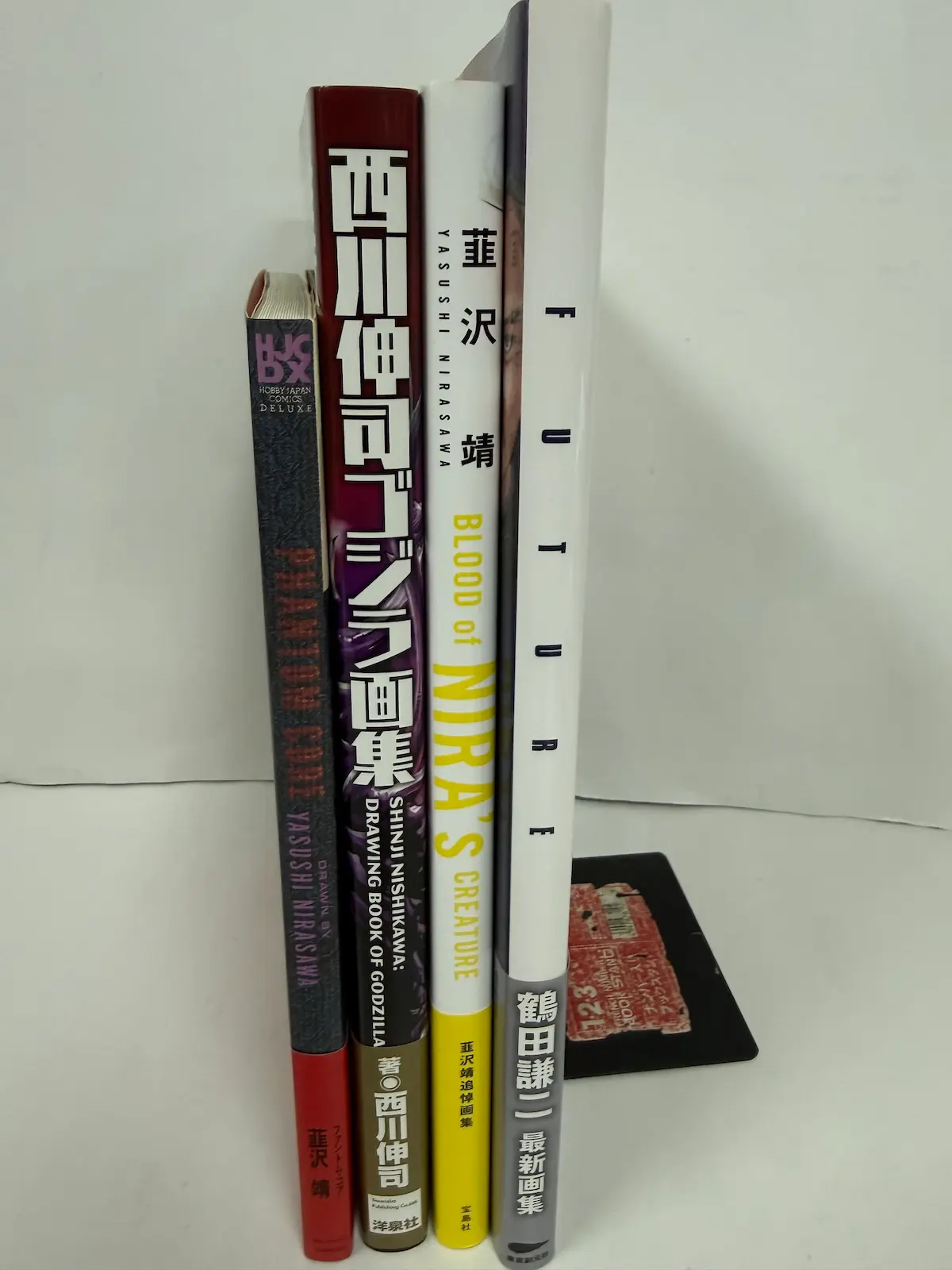 クリーチャー・怪獣デザインの画集4冊——韮沢靖『PHANTOM CORE』（HOBBY JAPAN COMICS DELUXE）、『西川伸司ゴジラ画集 SHINJI NISHIKAWA: DRAWING BOOK OF GODZILLA』（洋泉社）、韮沢靖『BLOOD of NIRA'S CREATURE』追悼画集（宝島社）、鶴田謙二『FUTURE』最新画集（東京創元社）の背表紙