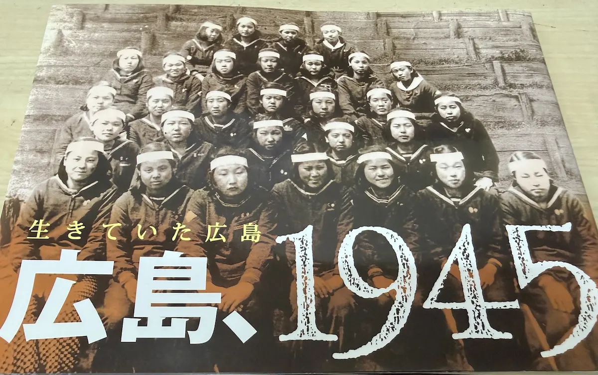南々社編『広島、1945——生きていた広島』（南々社・2012年8月6日発行）の表紙。セピアがかったモノクロの集合写真、鉢巻きを締めたセーラー服の女学生たちが正面を見つめている。上部に金色の小さな文字で「生きていた広島」、白抜きの大きな文字で「広島、1945」の題字