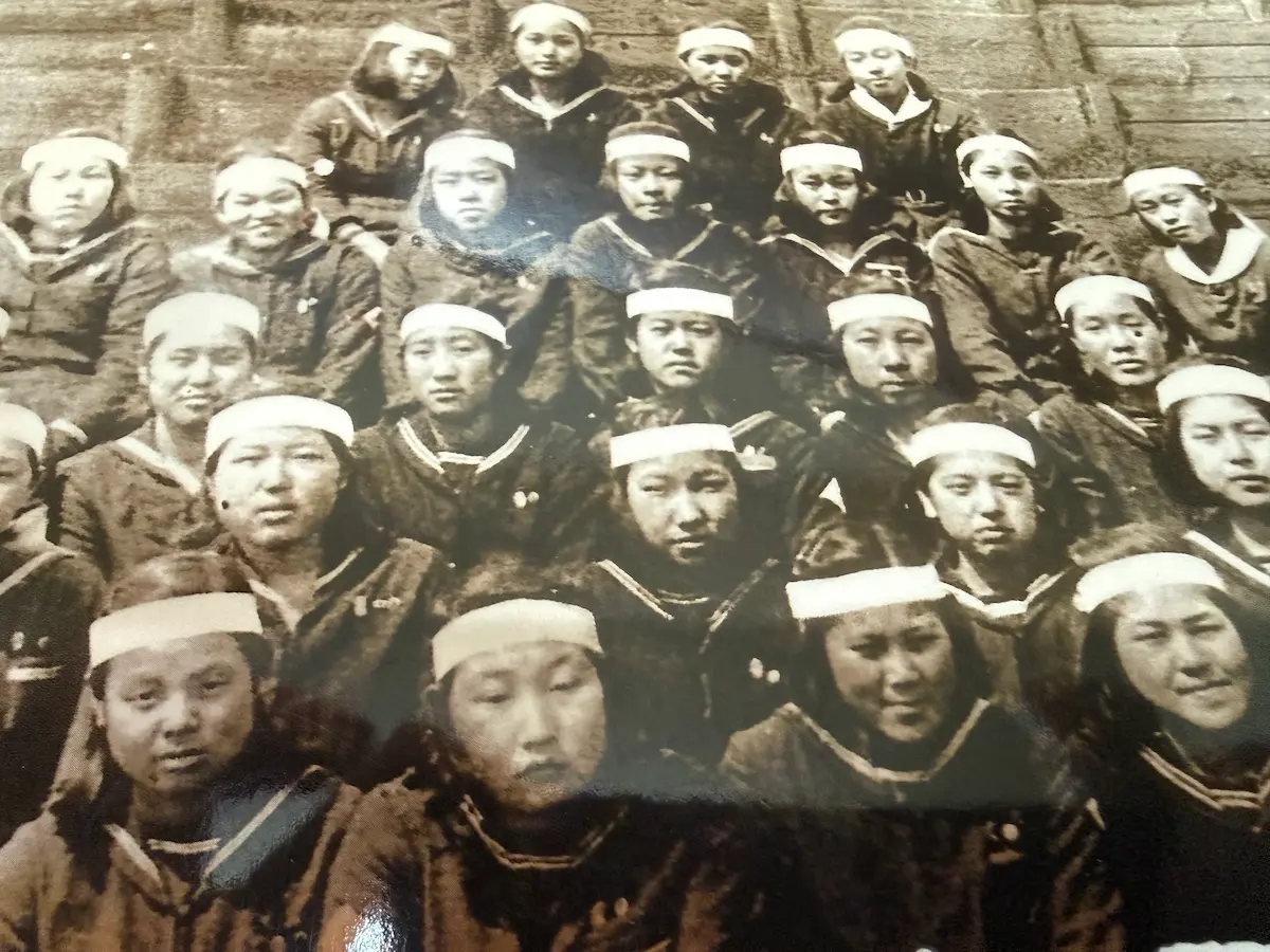 南々社『広島、1945』の表紙集合写真を寄って撮影したもの。鉢巻きを締めたセーラー服の女学生たちが4段に整列している。前列は膝の上で手を組み、中列・後列は正面を見つめる。1945年3月、動員先の東洋工業（現マツダ）で行われた広島女学院高等女学校の卒業式