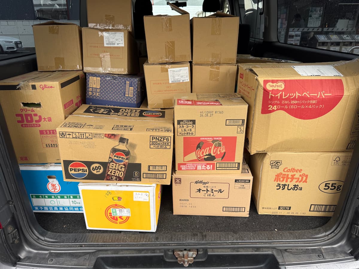 ハイエースの荷台に積まれた段ボール群。グリコ「クリームコロン大袋」箱、ペプシ「BIG ZERO」600mlペット24本箱、コカ・コーラ1.5L×6箱、カルビー「ポテトチップス うすしお味」55g箱、Kellogg'sオートミールごはん箱、TANOSEEトイレットペーパー24ロール箱、東予園芸農業協同組合の桃の青箱など、さまざまな流通用空き箱を活用して本を梱包した状態。
