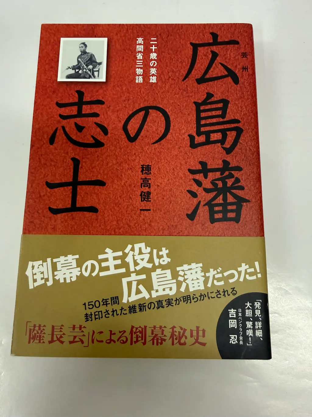 穂高健一『広島藩の志士 二十歳の英雄・高間省三物語』（南々社）の表紙。赤い地に黒い大きな文字で「広島藩の志士」、右上に小さく「芸州」。左上に椅子に座った洋装の若い武士の写真と「二十歳の英雄 高間省三物語」の副題。下半分の金色の帯に白抜きで「倒幕の主役は広島藩だった！」、続けて「150年間封印された維新の真実が明らかにされる」「『薩長芸』による倒幕秘史」、日本ペンクラブ会長 吉岡忍の推薦文「発見、詳細、大胆、驚嘆！」