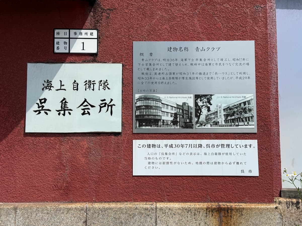 青山クラブ壁面に掛けられた呉市公式案内板と「海上自衛隊 呉集会所」のプレート、そして「種目 事務所建 / 建物番号 1」の金属プレート。案内板本文には青山クラブの概要（明治36年竣工、昭和11年建て替え、戦時中は海軍と市民をつなぐ交流の場、戦後昭和31年まで英連邦占領軍「呉ハウス」、昭和33年から平成29年まで海上自衛隊厚生施設、平成30年7月以降呉市が管理）と当時の古写真2枚（U.S National Archives所蔵、昭和20年(1945)と昭和38年(1963)）が掲げられている。下部には「この建物は、平成30年7月以降、呉市が管理しています。建物には耐震性がないため、地震の際は建物から必ず離れてください。呉市」の警告文。