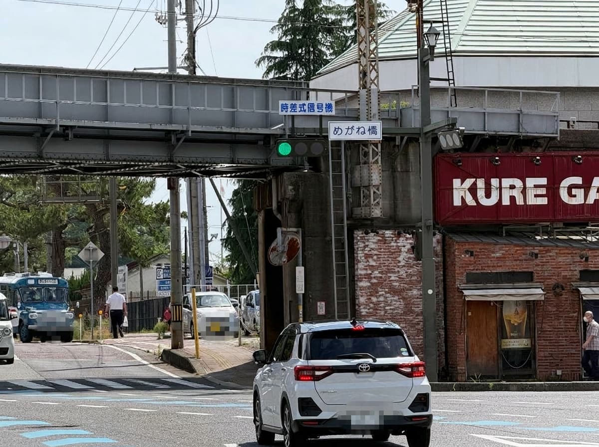 呉市・めがね橋交差点——時差式信号機の上に『めがね橋』の標識、右に赤レンガ調の小ビル『KURE GATE』、左に大和ミュージアム周遊バスツアー「れんがどおりコース」のボンネットバス