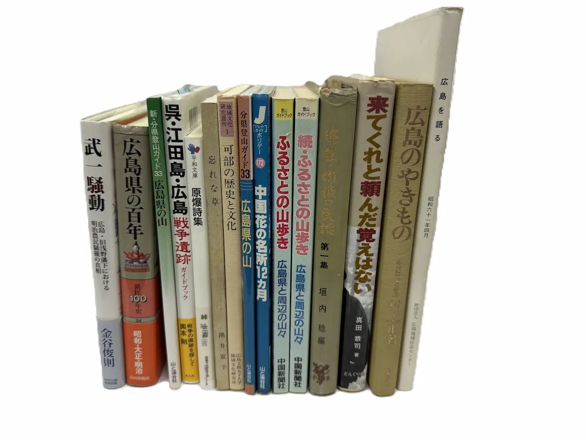 広島市南区でお譲りいただいた広島の郷土史15冊を、背を手前に向けて立てて並べた状態。左から武一騒動、広島県の百年、新・分県登山ガイド33 広島県の山、呉・江田島・広島 戦争遺跡ガイドブック、原爆詩集、忘れな草、可部の歴史と文化、分県登山ガイド33 広島県の山、中国花の名所12カ月、ふるさとの山歩き、続ふるさとの山歩き、安芸・備後の民話、来てくれと頼んだ覚えはない、広島のやきもの、広島を語るの背が並んでいる