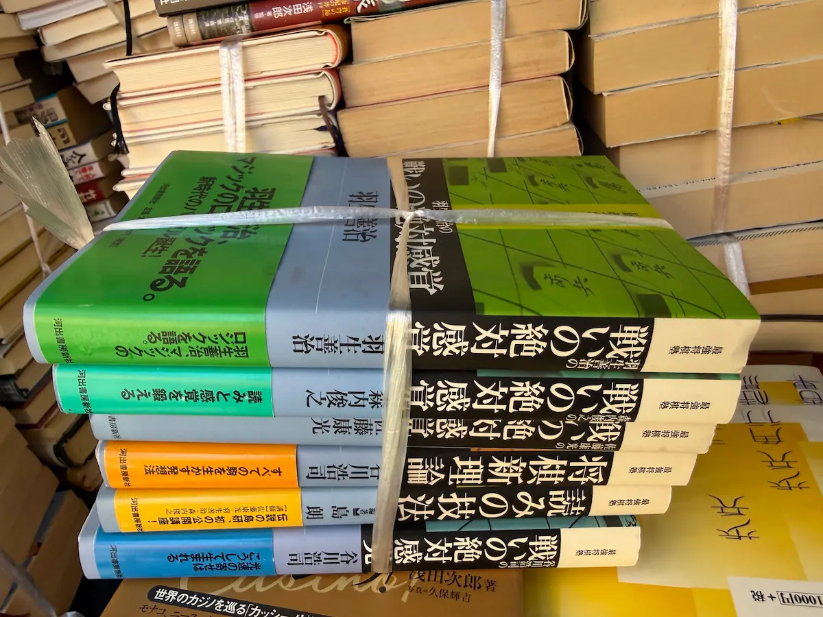 広島市南区でお預かりした河出書房新社「最強将棋塾」シリーズ6冊の紐で縛られた束。黒い背表紙に羽生善治・森内俊之・佐藤康光・谷川浩司それぞれの『戦いの絶対感覚』、谷川浩司『将棋・新理論』、島朗『読みの技法』が並び、左側には緑・青・オレンジ・黄の表紙が見えている