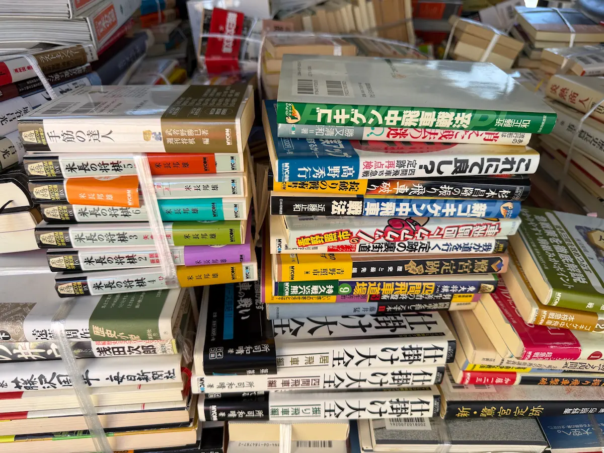 広島市南区でお預かりした米長邦雄『米長の将棋』全6巻（MYCOM）の紐で縛られた束。オレンジ・紫・緑・黄・青と色分けされた背表紙に1から6の巻数が並び、束の最上部には武者野勝巳『手筋の達人』（週刊将棋編・MYCOM）が置かれている。下段には所司和晴『仕掛け大全』の居飛車編・四間飛車編・振り飛車編が横積みされている