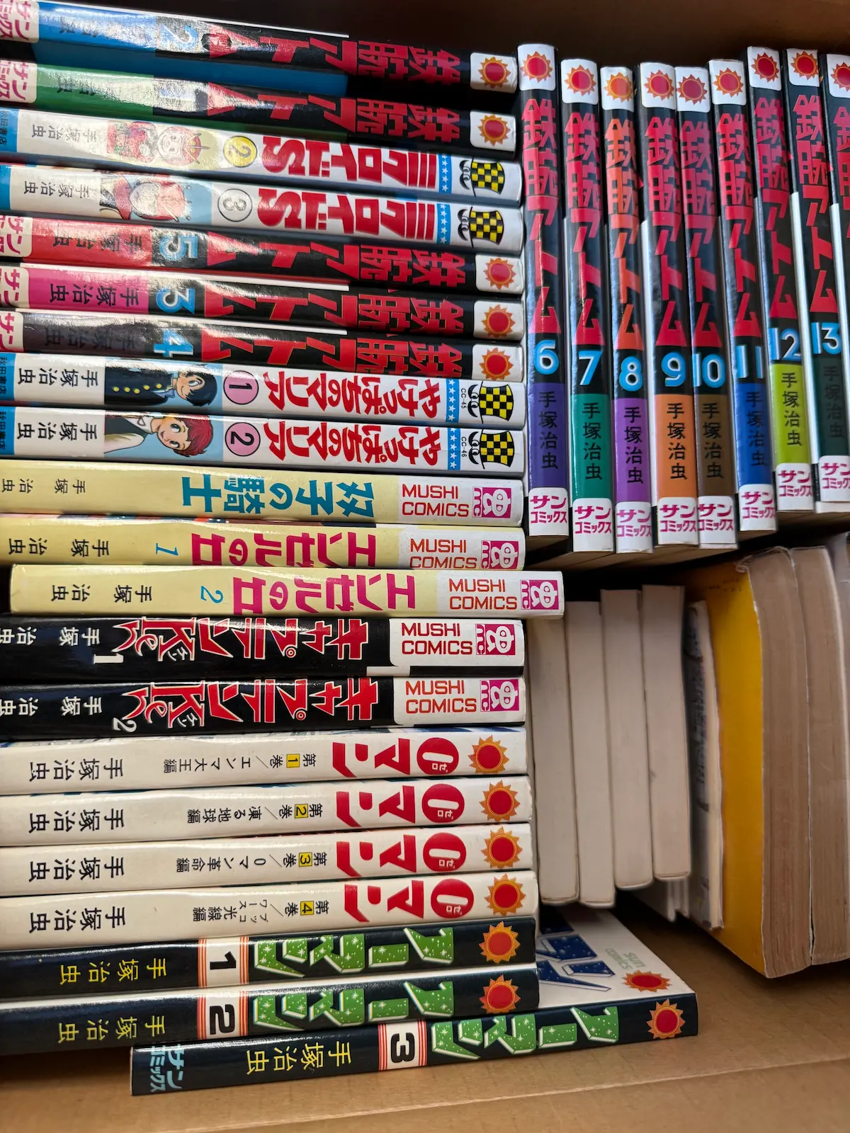 手塚治虫『鉄腕アトム』サンコミックス・虫プロコミックス版、『ミクロイドS』『やけっぱちのマリア』『ノーマン』『アラバスター』ほかが箱に詰められている様子